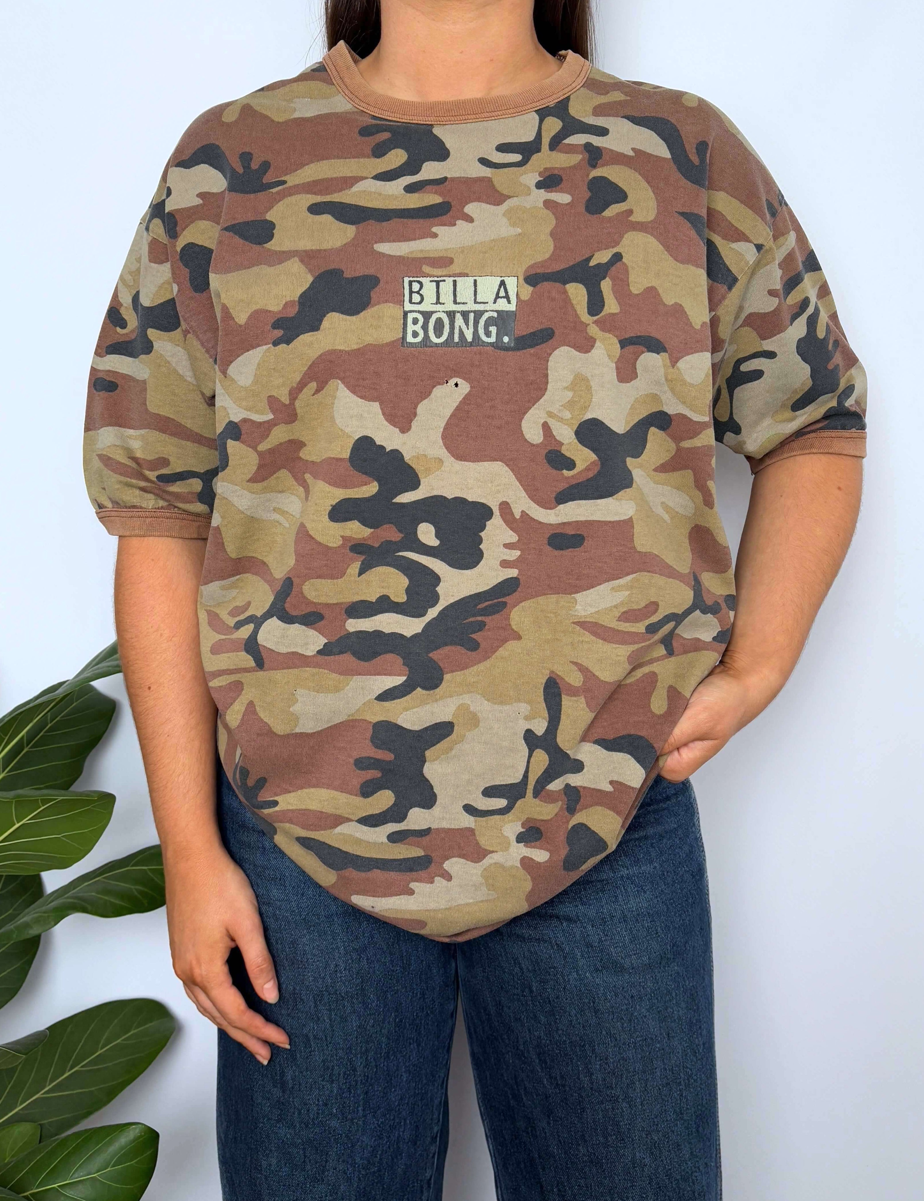 Person wearing a camouflage t-shirt with 'Billa Bong' logo against a white background