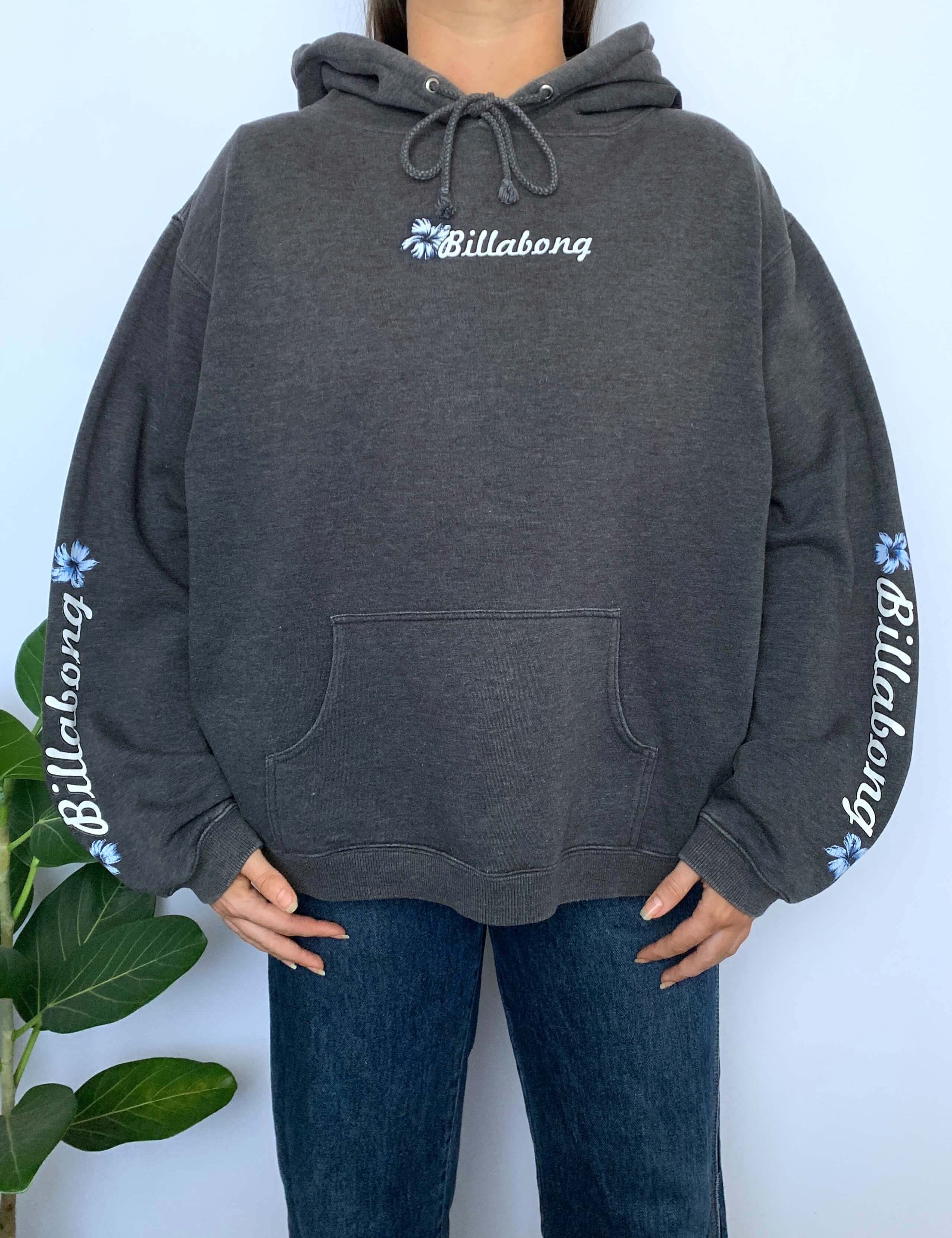 Person wearing a grey hoodie with Billabong spellout and flower logo on a white background