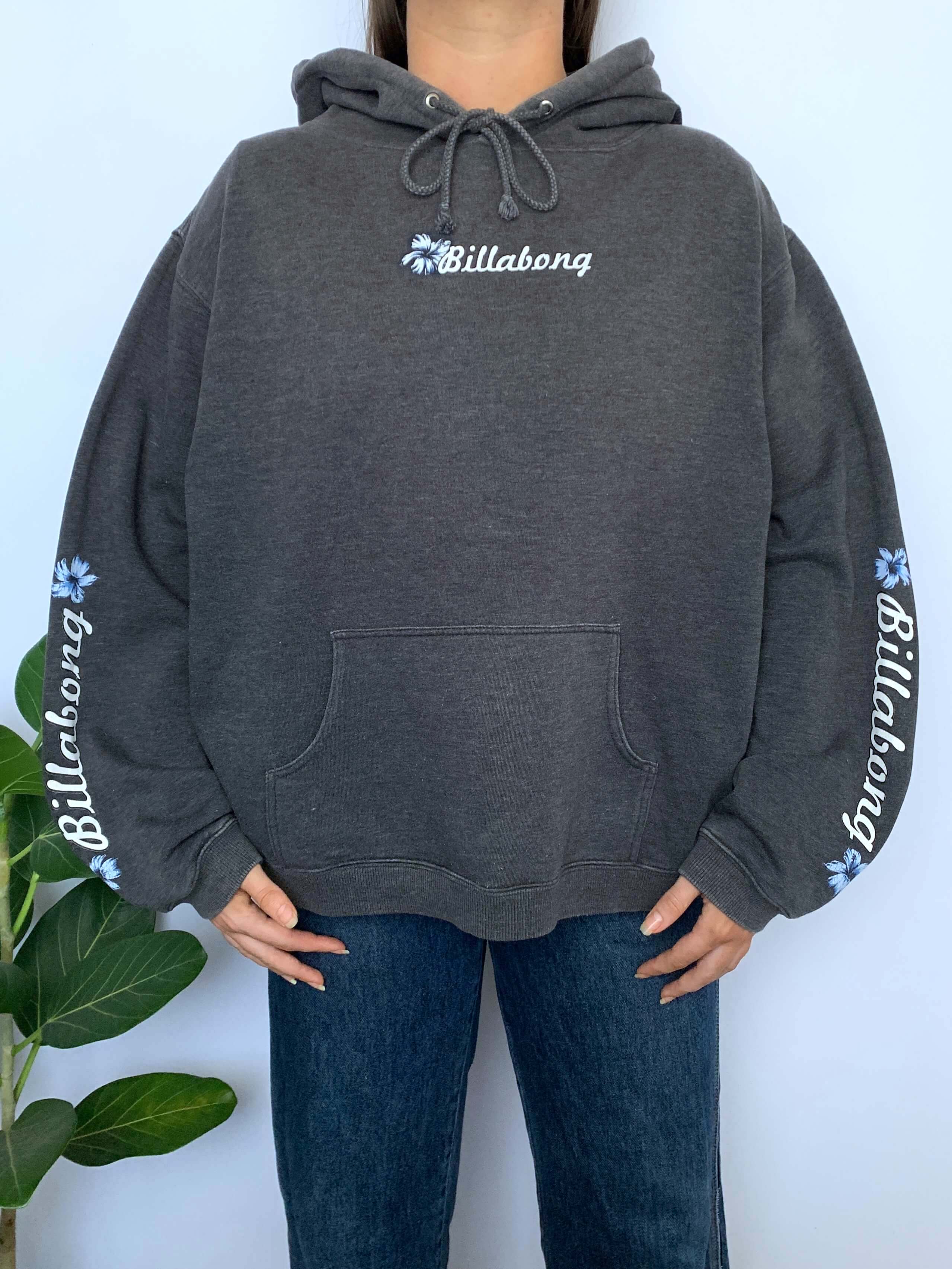 Person wearing a grey hoodie with Billabong spellout and flower logo on a white background