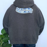 Person wearing a grey hoodie with 'Billabong' logo on the back against a white wall.